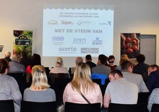 Deelnemers aan het Flandria Groentevakman/vrouw Seminarie nemen plaats, de sponsoren van de Groentevakman/vrouw staan geprojecteerd op de muur van de collegezaal.