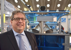 Roland Witvoer van GKS Packaging staat voor een machine die ervoor zorgt dat wortelen tijdens het verpakken minder schade oplopen. Boven de machine is in de spiegel een zwart rond gat te zien. Wanneer de wortelen normaal gesproken vanuit de wegers naar beneden vallen om afgevuld te worden, kunnen de puntjes beschadigen. Deze machine breekt de val halverwege, doordat het zwarte gedeelte in de weerspiegeling dicht blijft en later pas opengaat om de val te breken.