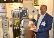 Erik de Roos van Bandall toont een label dat bedrukt kan zijn door een machine zoals achter hem. Op de standaardverpakkingen, drukt de machine extra informatie. De machine wordt vooral gebruikt wanneer er een product is met verschillende smaken, zoals de verpakking met aardappeltjes die Erik vast heeft. Wanneer de aardappelen bijvoorbeeld ook met rozemarijn verkocht worden, zet de machine op de voorkant en bij de ingrediënten van de standaardverpakking dat het gaat om een variant met rozemarijn.