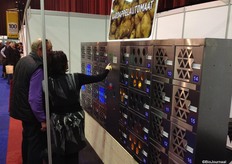 De Patatomat (aardappelautomaat) van het Vlaamse WDM wordt gedemonstreerd aan een bezoeker. De verlichte vakken laten zien dat het product aanwezig is. In de vakken kunnen aardappelzakken van 10 kg.